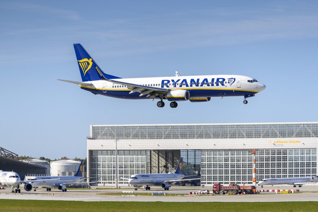 Aeropuesto con dos aviones parados y un avión despegando de Ryanair.